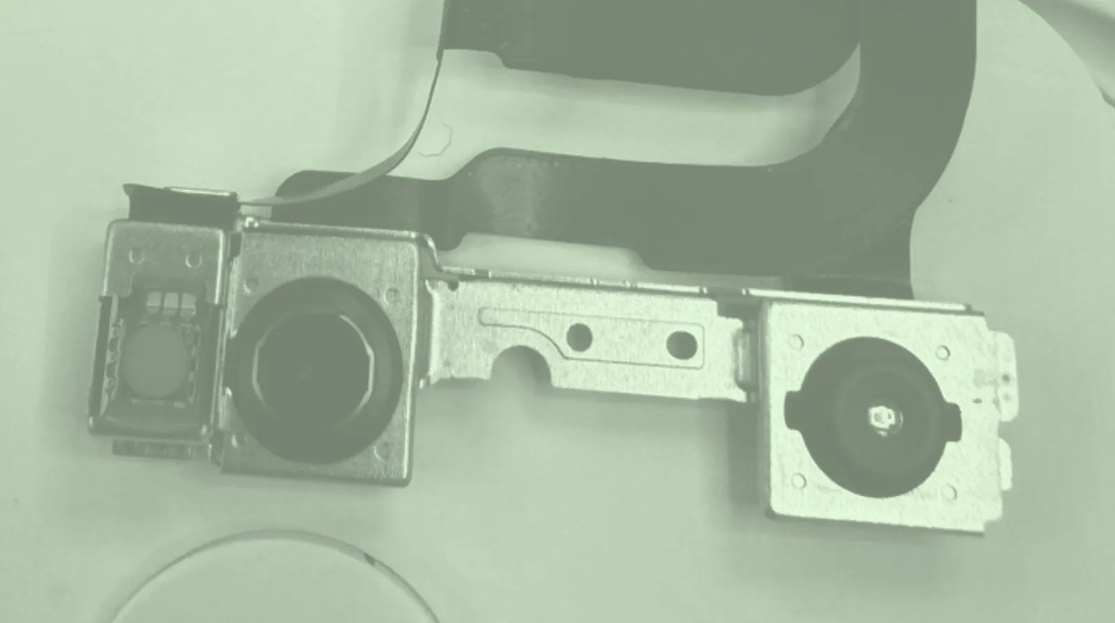 An iPhone front camera and Face ID sensor module, removed from the phone on its ribbon cable, tinted pale green